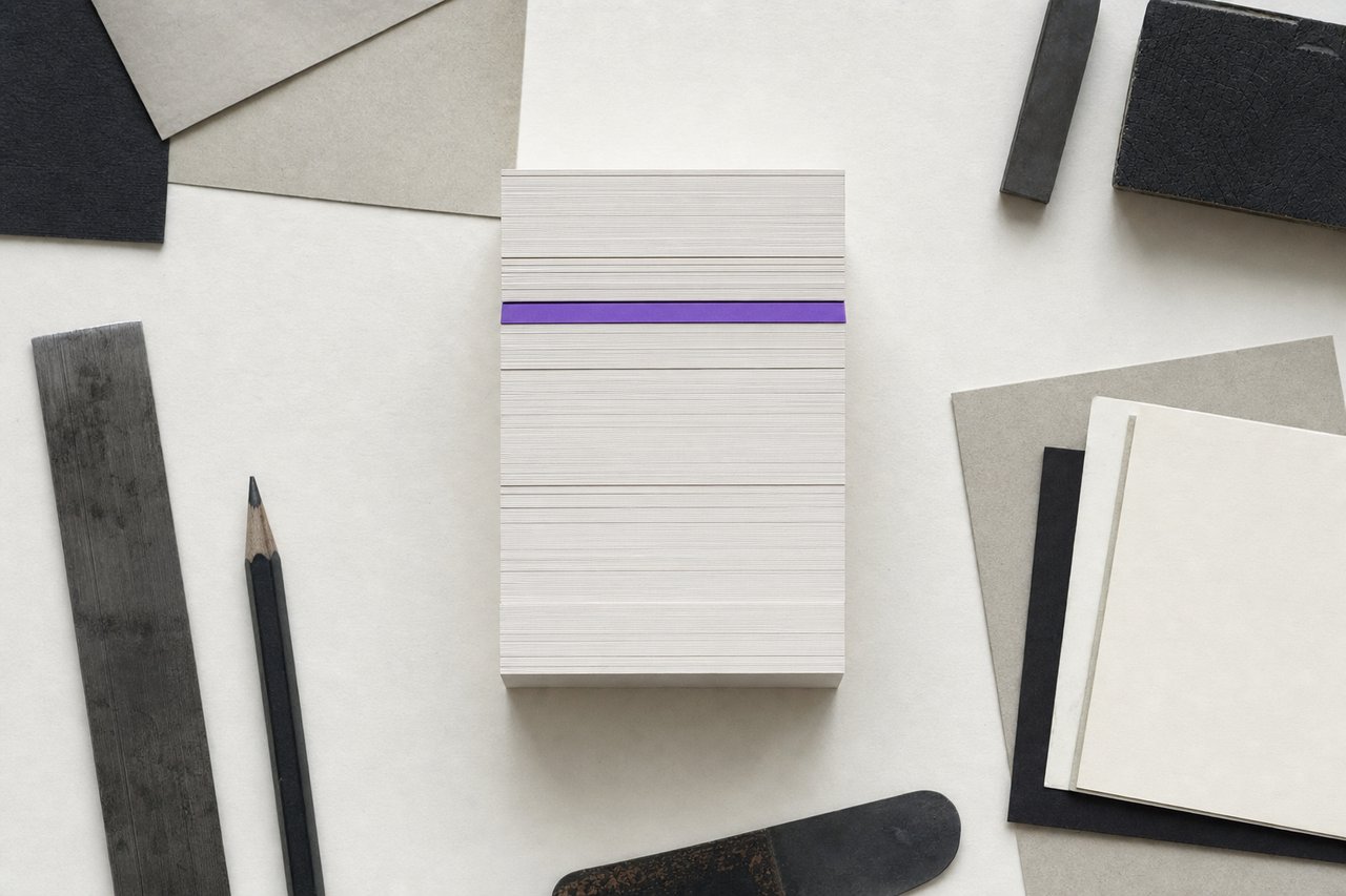 A tall stack of identical blank printed cards squared perfectly flush, one violet card inserted a third of the way down.