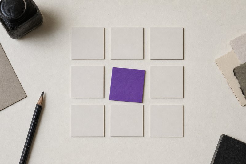 Nine identical small blank tiles laid in a three-by-three grid with equal gaps, one rotated slightly out of alignment and violet.