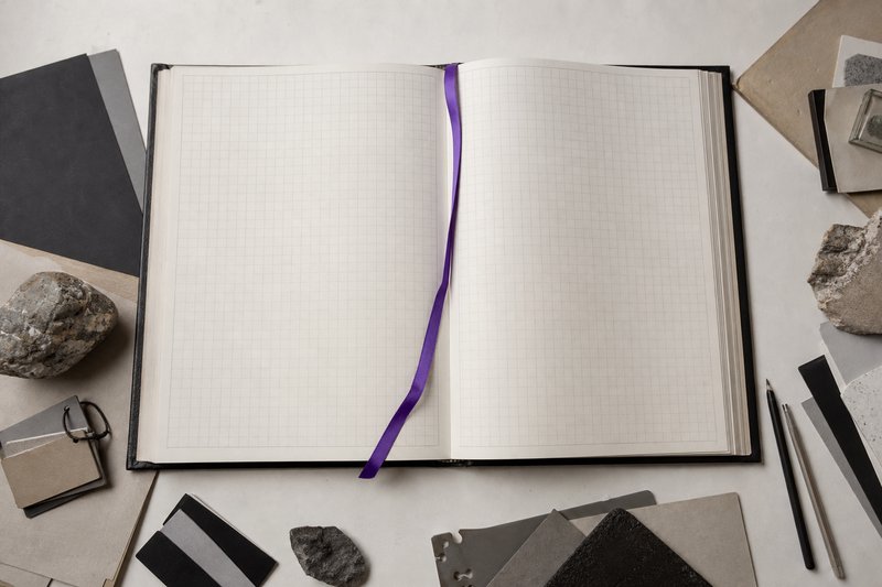 An oversized specimen album lying open at a blank ruled grid page, a violet ribbon marker across the gutter.