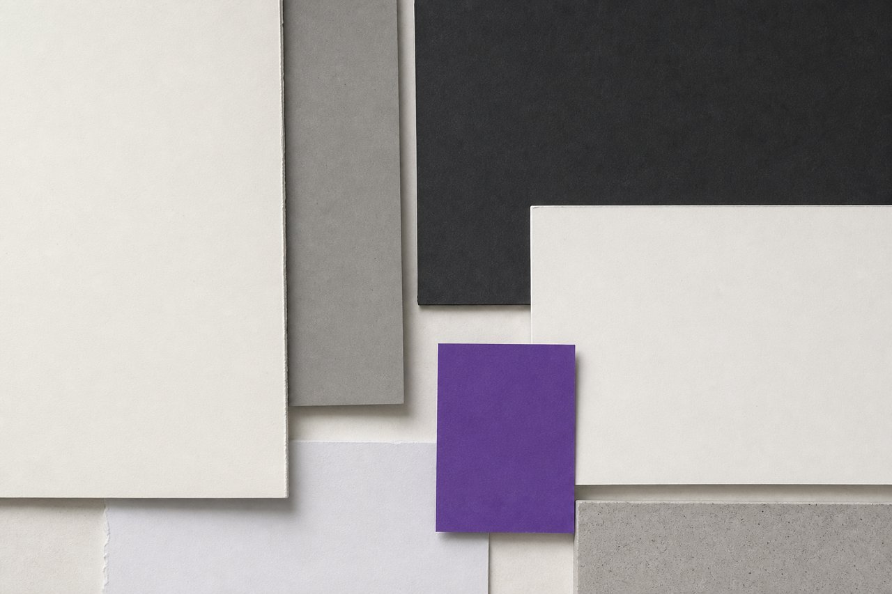 A blank foam-core presentation board leaning against a plain studio wall on a bare floor, a violet card at its base.
