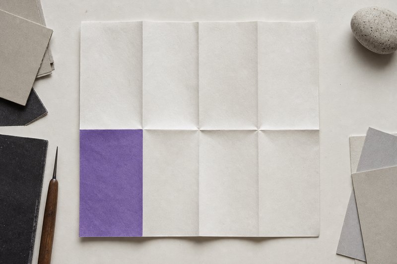 A large sheet of paper folded into a grid of creased rectangles and opened flat again, one rectangle shaded violet.