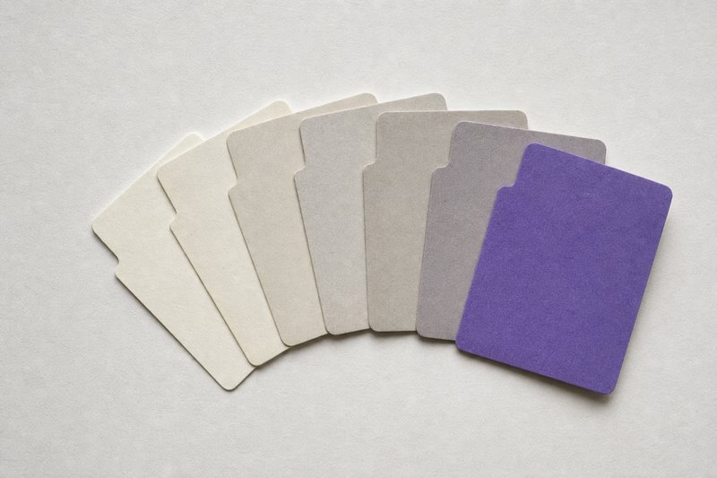 A row of blank paper index tabs fanned in a shallow arc, graduated from bone white to warm grey.